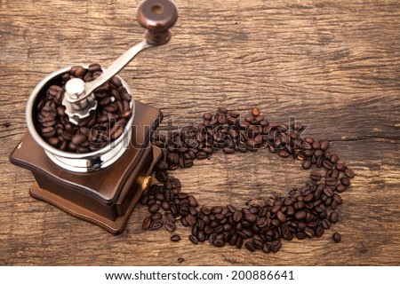 Vintage coffee bean grinder next to circle shape coffee beans on wooden table top as background