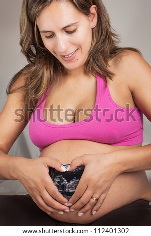 Happy Pregnant Woman Making a Heart with her Hands over the Ultrasound Exam Result