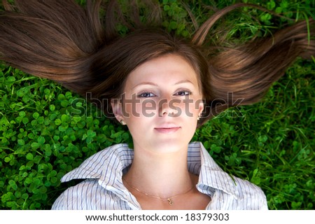 Young nice girl lying on the green grass with brown hair