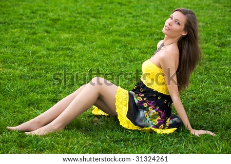 Young beautiful woman sitting in green grass in sun-dress