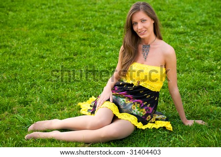 Young beautiful woman sitting in green grass in sun-dress