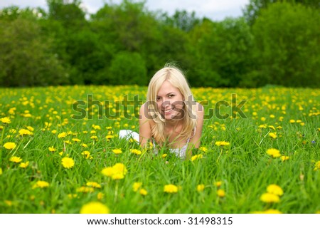 Young beautiful woman relaxing on a green meadow with dandelion