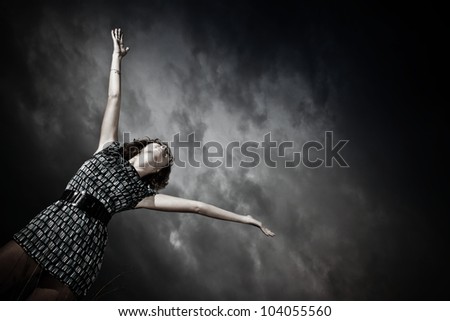 Girl looking up and stretching her arms towards the cloudy sky outdoors