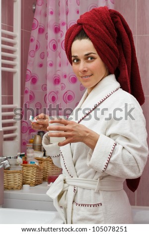 Portrait of a beautiful young woman standing in her bathroom in a robe, with towel on head, preparing to brush her teeth, smiling into camera