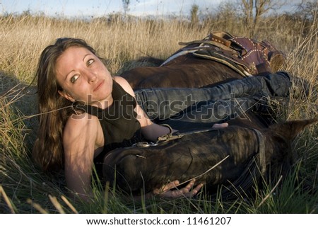 young woman and her black horse laid down in a field