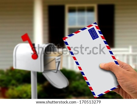 Hand Holding Envelope in Front of a House