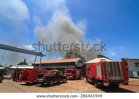Fire truck and burning warehouses with black smoke against blue sky