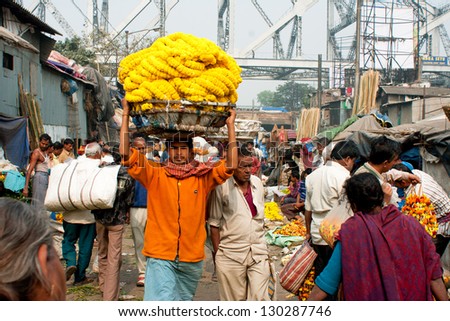 KOLKATA, INDIA - JAN 13: Worker with a cart on the head rush on the crowded Mullik Ghat Flower Market on January 13, 2013 in Kolkata. The market is 125 years old. 2000 sellers work in it every day.