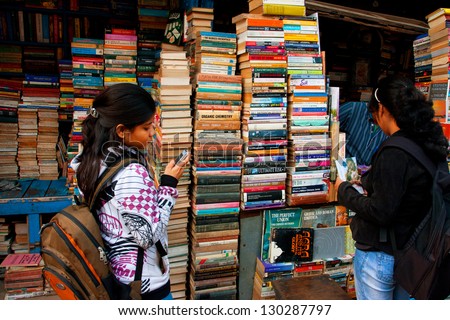 KOLKATA, INDIA - JAN 15: Young female student with a cell phone choose the book on the street market on January 15, 2012 in Kolkata. From 1976 Kolkata have the Book Fair with 2 million visitors annual