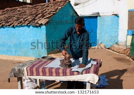 ORCHHA, INDIA - DEC 20: Asian man irons clothes by the coal iron outdoor at the sunny day on December 20 2012 in Orchha, Madhya Pradesh, India. Orchha had a population of 10000. Males constitute 53%