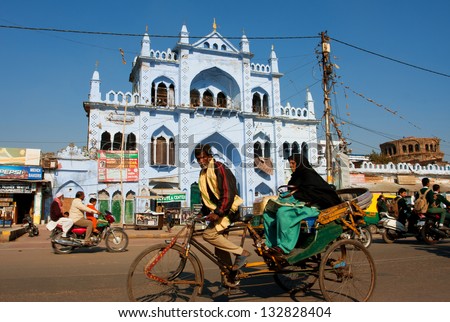 LUCKNOW, INDIA - DEC 18: Cycle rickshaw takes an elderly Muslim woman on a beautiful street with blue houses on December 18, 2012 in Lucknow India. Lucknow in Uttar Pradesh state has pop. of 4,588,455