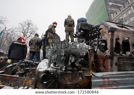 KYIV, UKRAINE - JAN 21: Men in helmets and masks stand on top of broken and burned military cars on occupying winter city during anti-government protest Euromaidan on January 21, 2014 in Kiev, Ukraine