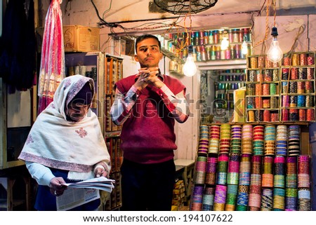 VARANASI, INDIA - JAN 4: Old man reading a newspaper near the young seller of the women\'s  jewelry on the market street on January 4, 2013. Varanasi urban agglomeration had a population of 1,435,113