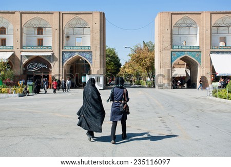 ISFAHAN, IRAN - OCT 14: Two women in traditional hijabs rushing from Imam Square with old bazaar on October 14, 2014. Naqsh-e Jahan or Imam Square constructed in 1598. UNESCO\'s World Heritage Sites