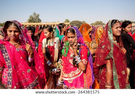 JAISALMER, INDIA - MAR 1: Beautiful women in red sari dresses going through the crowd to the popular Desert Festival on March 1, 2015 in Rajasthan. Every winter Jaisalmer takes the Desert Festival