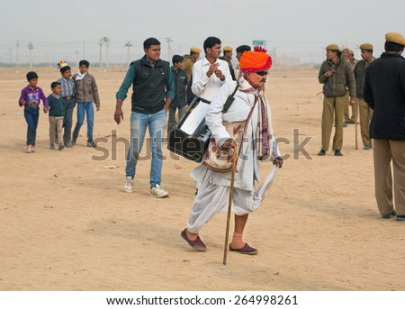 JAISALMER, INDIA - MAR 2: Old musician in sunglasses with a keyboard in a hurry at the Desert Festival on March 2, 2015. Every year in the february Jaisalmer takes the village Desert Festival