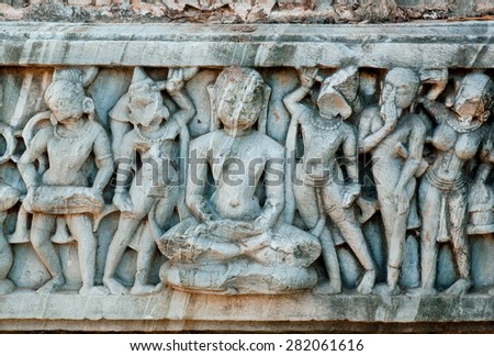 Buddha sitting in the crowd of people on the crumbling bas-relief. Wall of ancient temple in India
