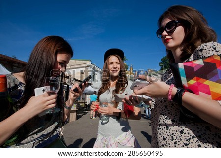 KYIV, UKRAINE - JUNE 6, 2015: Three cute young women with wine glasses and mobile phones talking during the Kiev Food & Wine Festival on June 20 2014. Ukrainian capital, Kiev has popul. near 2,900,200