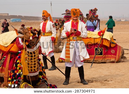 JAISALMER, INDIA - MAR 1: Indian man in old guardian uniform sending sms by mobile phone near camel of Desert Festival on March 1 2015 in Rajasthan. Every winter Jaisalmer takes the Desert Festival
