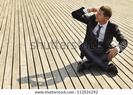 young businessman looking for job. He is sitting on wooden floor and wraps up  his face with the hand