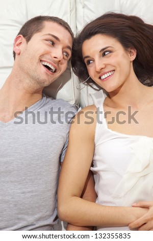 Young lovely couple together lying in a bed and listening music   / A smiling couple lying with headphones