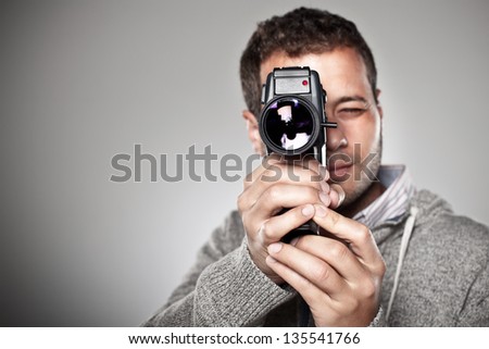 Man filming with a video camera. / Portrait of a normal man with video camera over grey background.