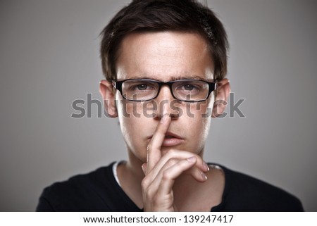 Attractive young man with rimmed glasses. In studio/ Portrait of a normal man with finger on lips keeping a secret