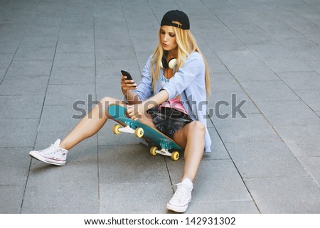 Young woman on the skater sending a message with a smart-phone / Skater woman in outdoors