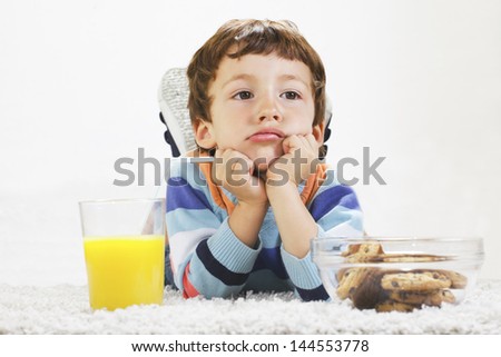Little boy with cookies and orange juice stretching on carpet./ Angry child with breakfast in home.
