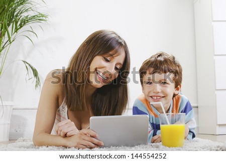 Mother and child on a carpet stretched with pad and orange juice./ Mother and son having fun with a digital tablet in home