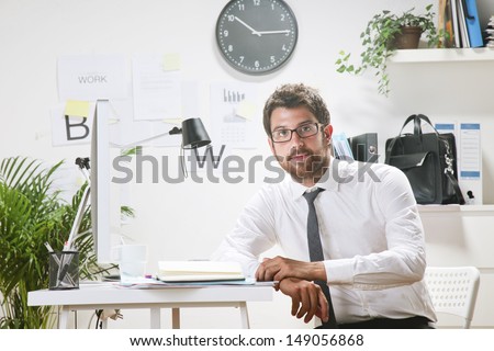 Young businessman in office looking at camera. Businessman with rimmed glasses working.