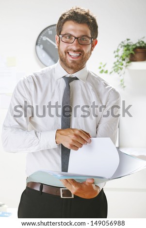 Young businessman smiling and subject some papers in office. Businessman with rimmed glasses looking at camera.