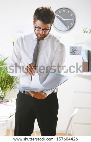 Businessman with rimmed glasses working./ Young businessman looking some papers in office.