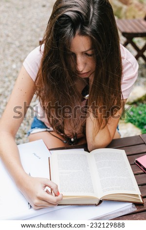 Young beautiful female sitting outside and studying hard. / Young woman doing homework on the home garden.