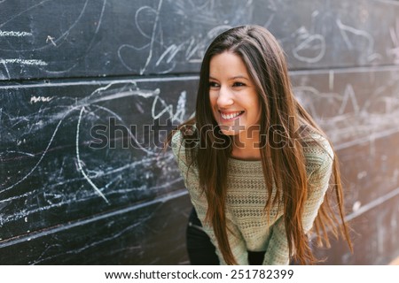 Happy young woman looking at camera. / Young beautiful woman standing in front a blackboard wall.
