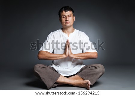 Peaceful man doing yoga and meditating over dark background