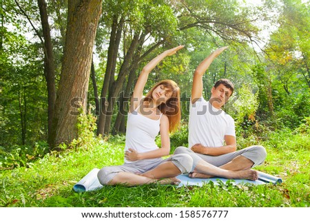 Young man and woman doing yoga. Lotus pose meditation in a garden. Outdoor full body