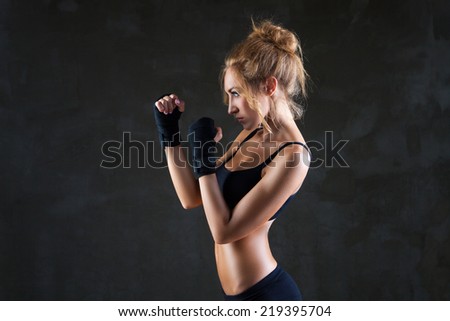 Young beautiful sexy boxer woman making kick with boxing bandage on hands over grey background