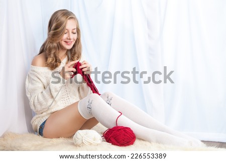 Portrait of charming girl in sweater sitting on windowsill and knitting
