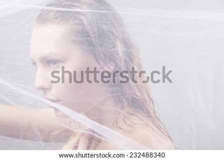 Close-up of beautiful wet woman face with waving fabric over light grey background