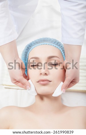 Woman getting face treatment in medical spa center, cleansing with cosmetic cotton pads