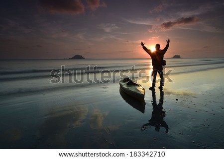 a silhouette man with kayak enjoy a sunrise near at beach, awesome reflection
