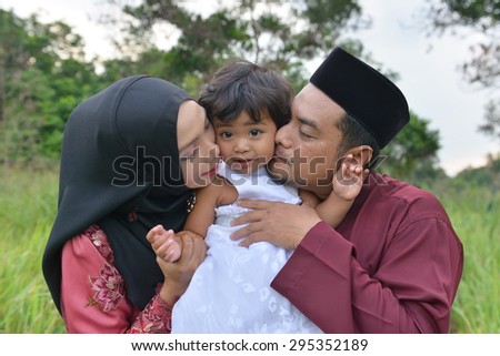 malay family having fun in the park ,malaysian people. Mother and father kissing his daughter.