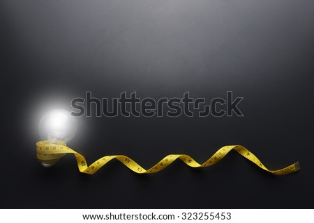 Lowlight key of light bulb and Yellow measuring tape with water drop on grey background