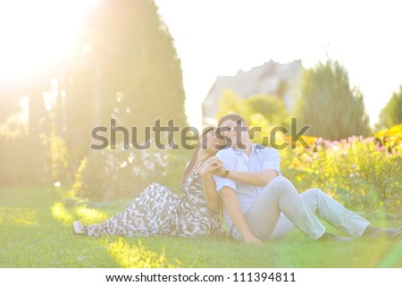 Young happy couple sitting back to back to each other - bright sunset time