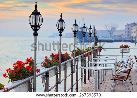 Street open cafe with view at the canal, Venice, Italy. Tables and seats are empty. Flowers decorate cafe. Cozy romantic evening place.