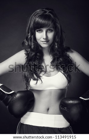 Young sexy girl over black background with boxing gloves. Black and white.