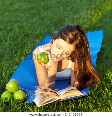 pretty young woman lying on green grass reading book with green apples