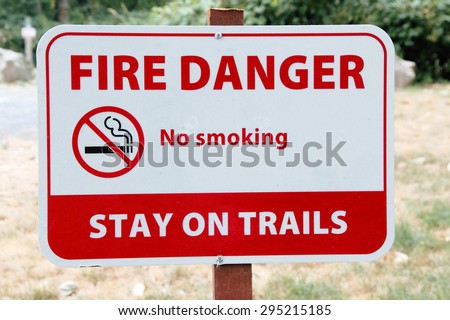 A sign warns that smoking on trails is forbidden/Fire Danger Sign/A public sign warns that smoking is forbidden on a nature trail.