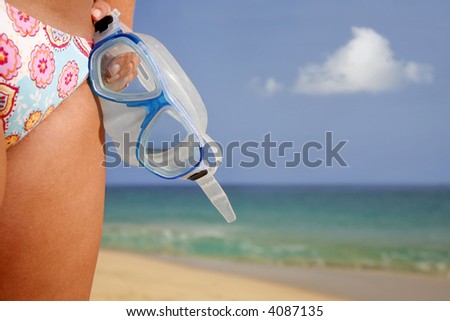 Woman in bikini by bright beach holding snorkel